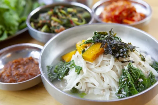 칼국수 — 단호박·김·푸른 잎채소 고명, 뒤로 반찬